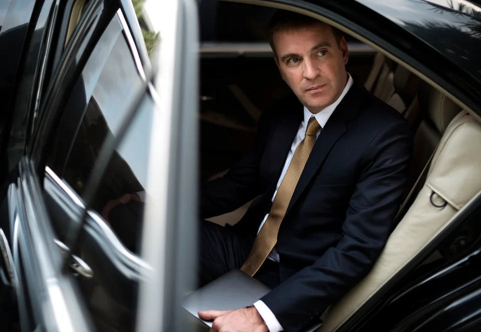 executive holding laptop in back seat of chauffeured luxury vehicle